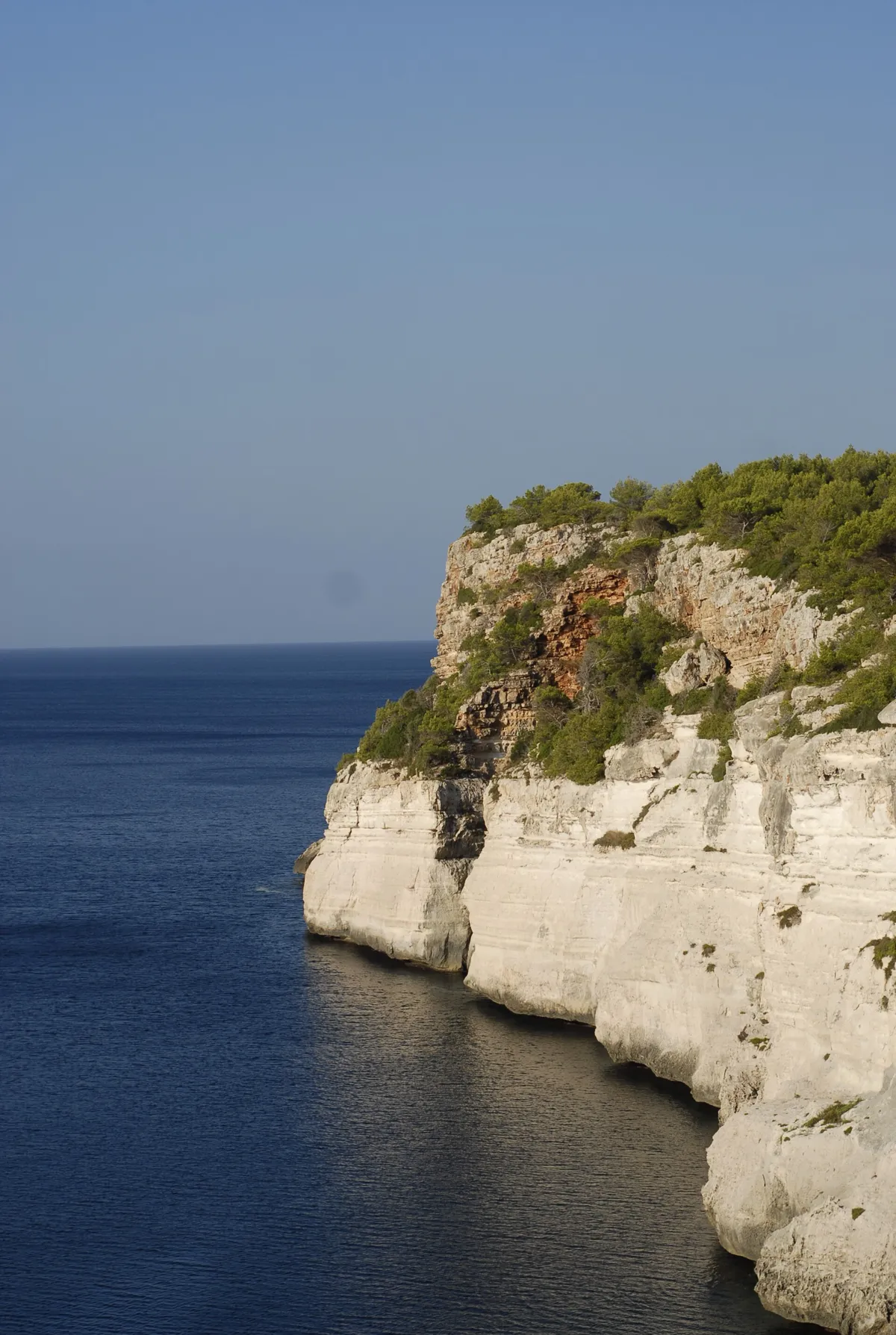 High limestone cliffs above the sea at Cala en Porter in Menorca near the cave line kayaks enter and boats pass