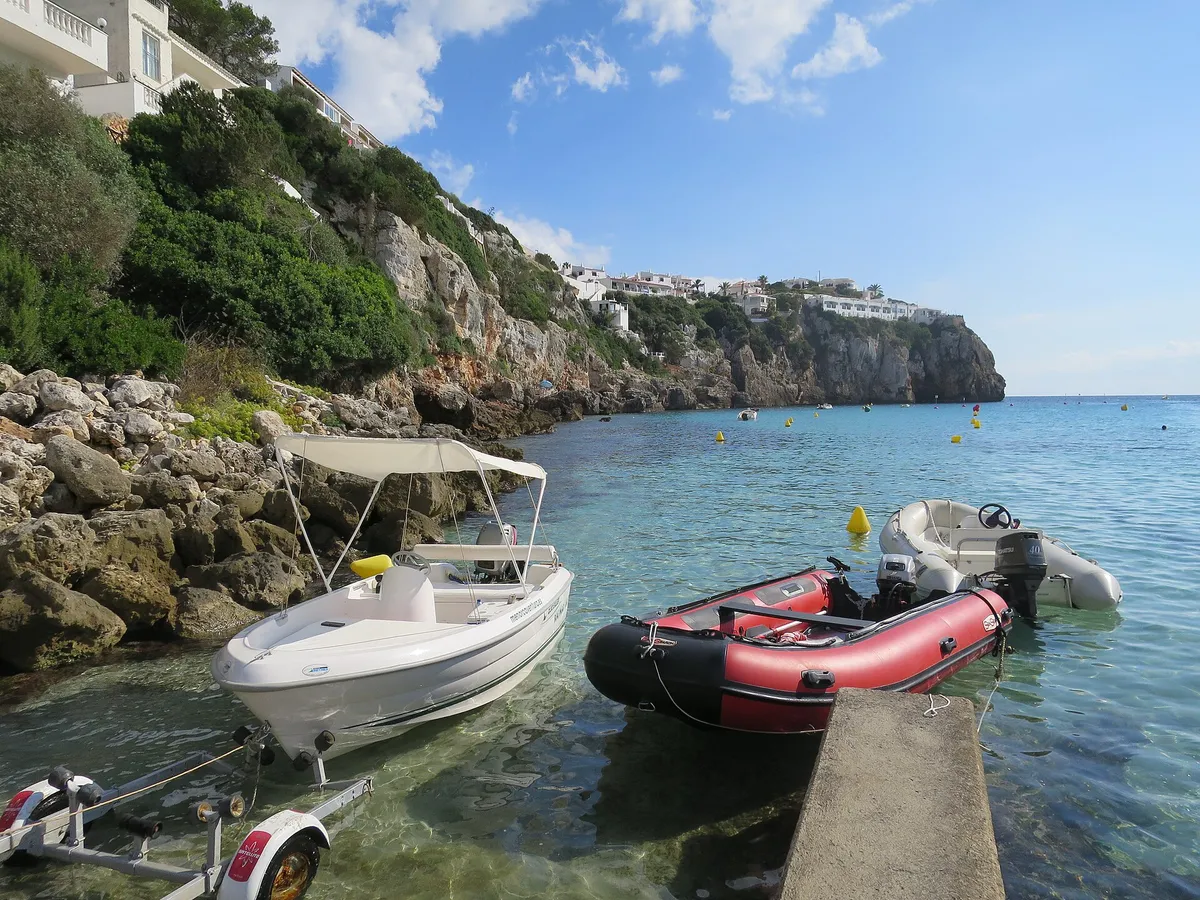 Small boats moored in the shallow clear water of Cala en Porter in Menorca, a sheltered family swimming cove